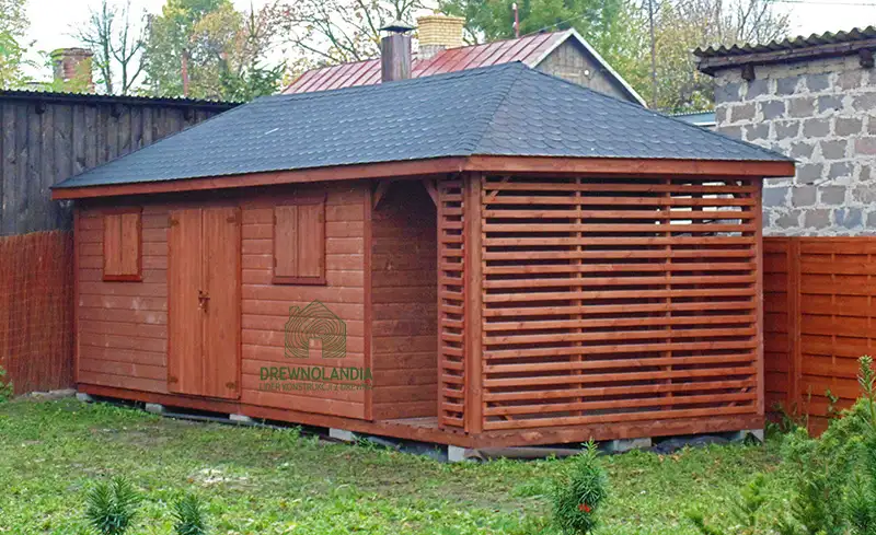 maly domek letniskowy stojący przy plocie z ciemnym dachem