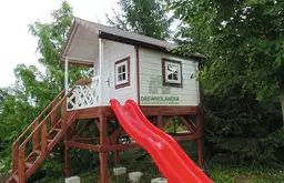 biały domek dla dzieci z czerwoną zjeżdżalnią