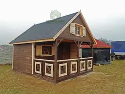 ciemnobrązowy domek letniskowy z czarnym dachem stojący przy płocie