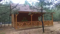 domek letniskowy z dużym tarasem i czerwonym dachem stojący wśród drzew